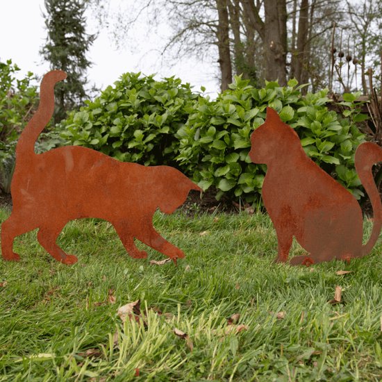 Twee roestkleurige metalen katten silhouetten in de tuin.