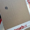 Bruine kartonnen doos met wit-rode tape van "web.nl" en een rond HEM-logo.