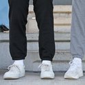 Zwart en grijs joggingbroek met witte sneakers en sokken, gedragen door twee personen op een trap.