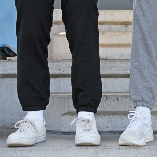 Zwart en grijs joggingbroek met witte sneakers en sokken, gedragen door twee personen op een trap.