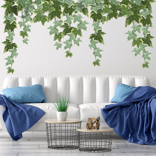 Des lianes de lierre vertes décorent le mur au-dessus d'un canapé blanc avec des coussins et des plaids bleus.