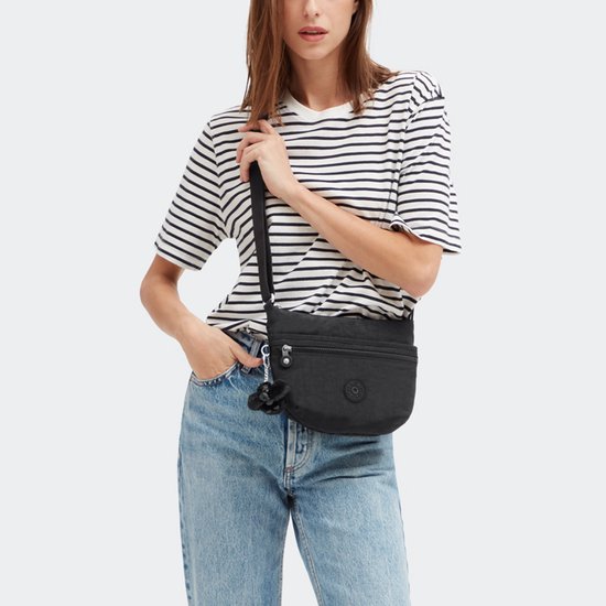 Model draagt een zwarte Kipling schoudertas over haar gestreepte shirt en jeans. De tas heeft een aapje.