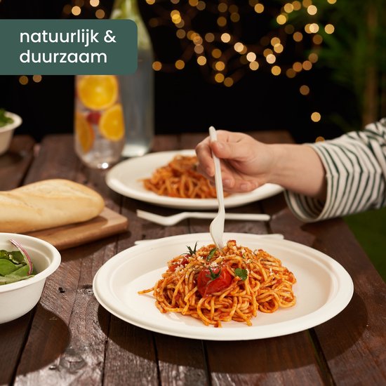Een bord met spaghetti, tomaat en kaas op een houten tafel met een fles water en achtergrondverlichting.