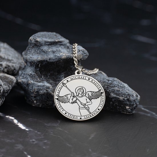 Zilverkleurige ketting met ronde engel hanger tussen grijze rotsen.