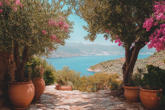 Pots en terre cuite flammée le long d'un chemin de pierre entre des oliviers en fleurs roses, surplombant une mer bleue et des collines.