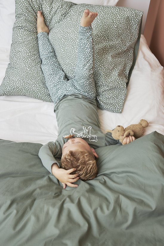 Jongen ligt op bed met een knuffel, gekleed in een pyjama met stipjes.