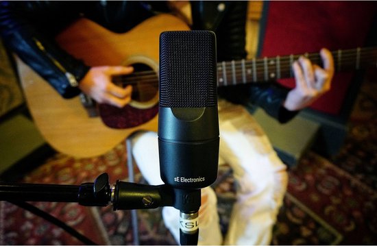 Persoon speelt akoestische gitaar in een studio, met zwarte sE Electronics microfoon op de voorgrond.