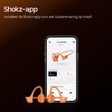 Oranje Shokz OpenRun Pro 2 Mini koptelefoon naast een smartphone met de Shokz app. De app toont EQ-modi.