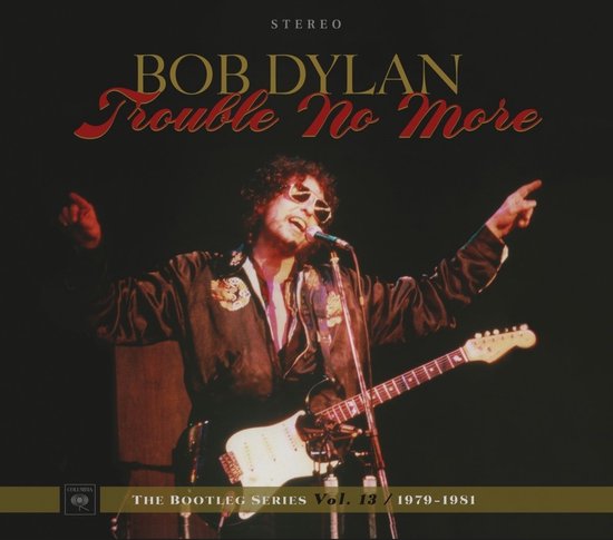 Bob Dylan met zonnebril en gitaar, wijzend naar het publiek, tekst 'Trouble No More'.