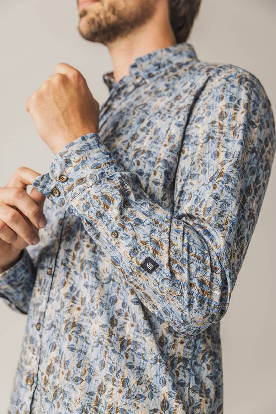 Man die zijn manchet van een blauw overhemd met bladprint aanpast.