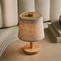 Tafellamp met linnen kap en houten voet, geplaatst op een bijzettafel.