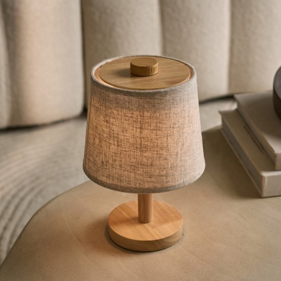 Tafellamp met linnen kap en houten voet, geplaatst op een bijzettafel.