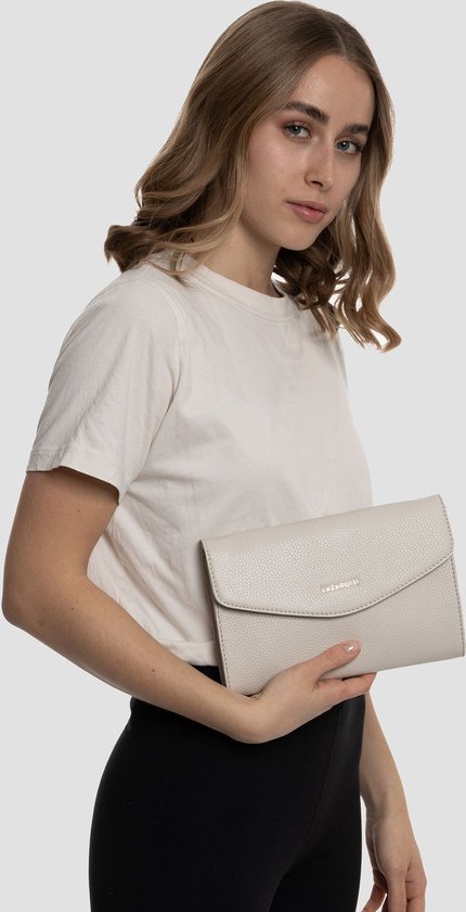 Crèmekleurige lederen clutch met goudkleurig logo, gedragen door een model met een witte T-shirt.