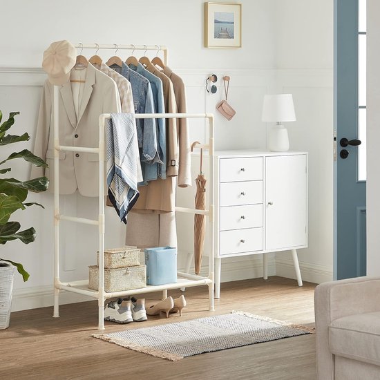 Kledingrek met een beige blazer, jeans, jas en accessoires in een lichte kamer.