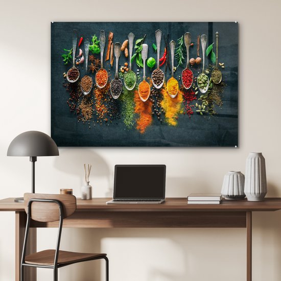 Glasschilderij met een rij zilveren lepels gevuld met kleurrijke kruiden en specerijen op een donkerblauwe achtergrond.