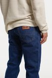 Man in spijkerblauwe Wrangler spijkerbroek, met bruine stiksels en een bruin leren label op de achterzak.