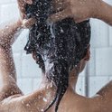 Vrouw met donker haar wast haar haar onder de douche met waterstralen.