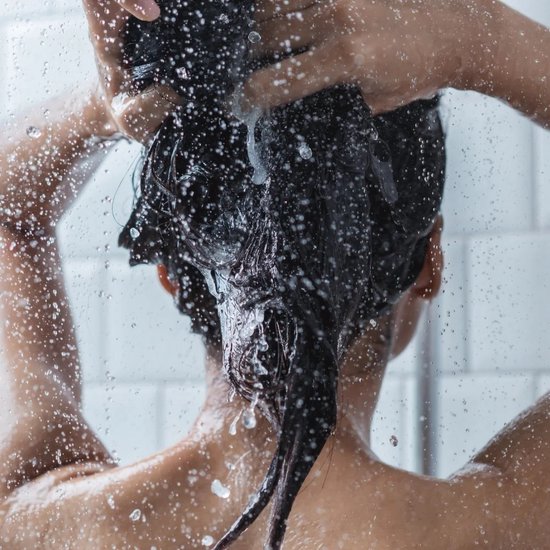 Vrouw met donker haar wast haar haar onder de douche met waterstralen.