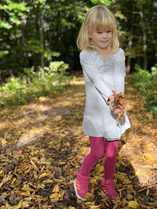 Lachend jong meisje met blonde haren in een grijs jurkje en roze maillot, vasthoudend herfstbladeren.