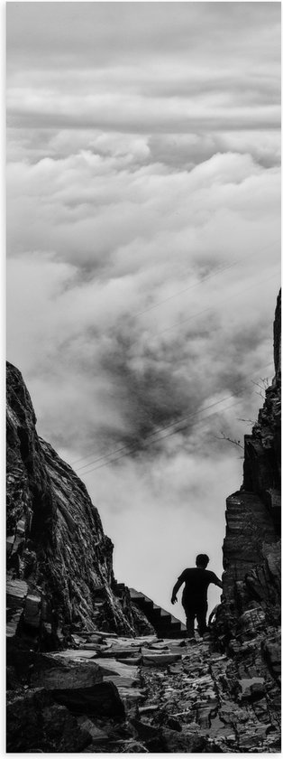 WallClassics - Poster Glanzend – Man tussen Rotsen boven Wolken in Zwart-wit - 20x60 cm Foto op Posterpapier met Glanzende Afwerking