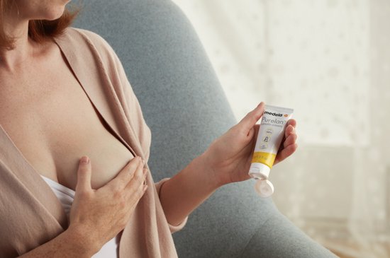 Vrouw houdt een tube Medela Purelan Lanolin cream vast, met haar borst zichtbaar.