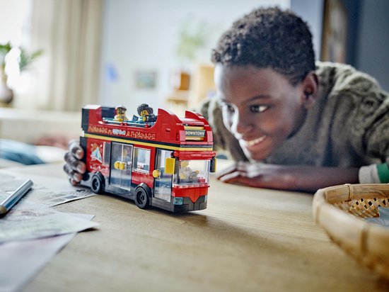 Jongen bekijkt een rode LEGO dubbeldekker bus met twee verdiepingen op een tafel.