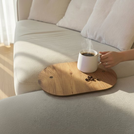 Ovaal houten banktafeltje op een beige bank, met een stomende witte mok en koffiebonen.