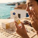 Vrouw brengt Nivea Sun Spot Control SPF 50+ gezichtszonnebrandcrème aan op het strand. Textuur 50+ UV Viso Specialist.