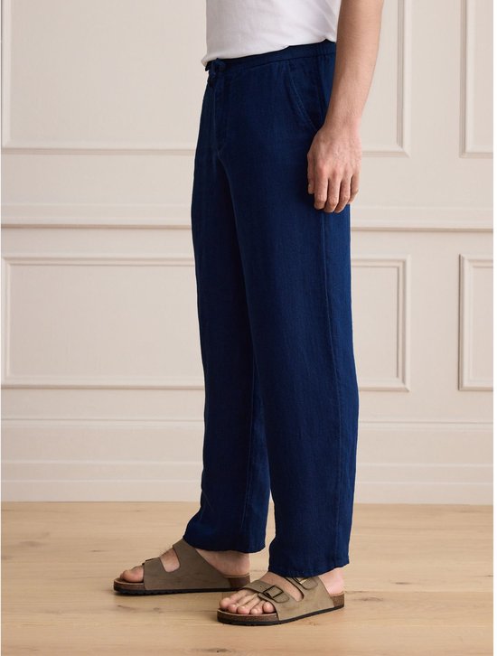 Zijaanzicht van de blauwe linnen broek met relaxte pasvorm, gedragen met een wit t-shirt en sandalen.