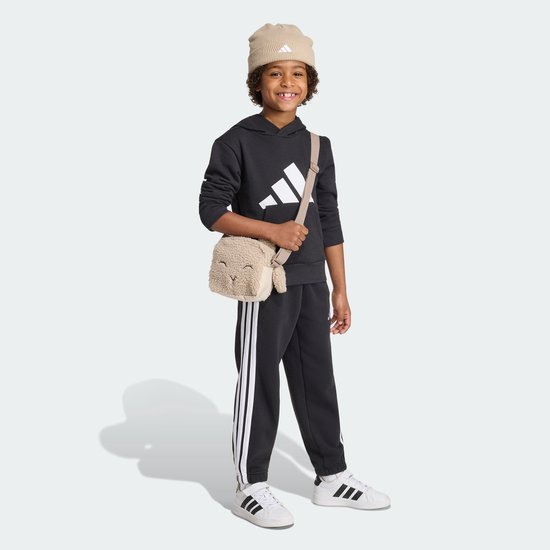 Jongen met een beige teddy tasje in de vorm van een schaapje, draagt een zwarte hoodie en broek.