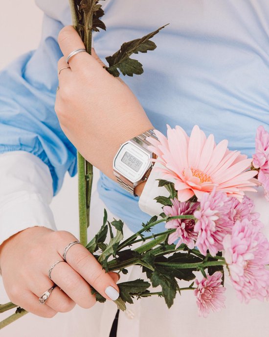 Zilverkleurig Casio horloge met digitale display gedragen door een vrouw met een blauwe blouse en bloemen.