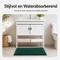 Donkergroene badmat voor een witte wastafelmeubel met zwarte deuren en een mand met handdoeken.