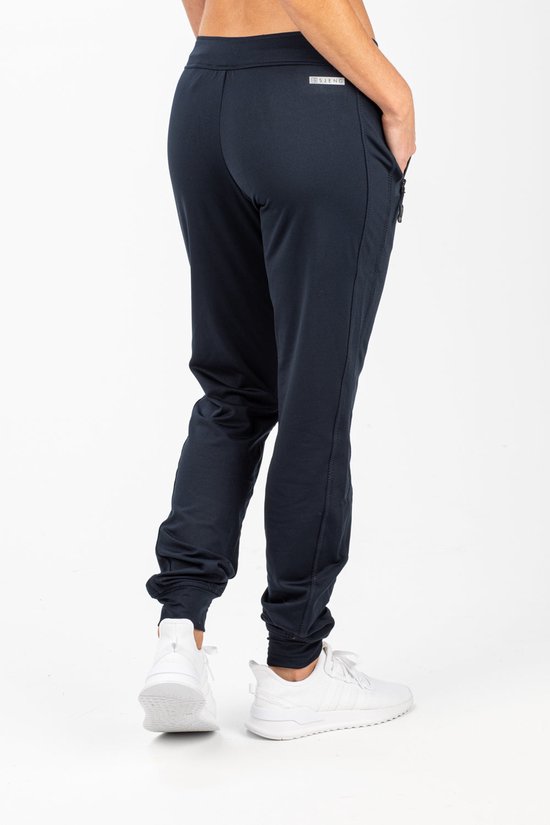 Model in donkerblauwe trainingsbroek van Sjeng Sport met witte sneakers.