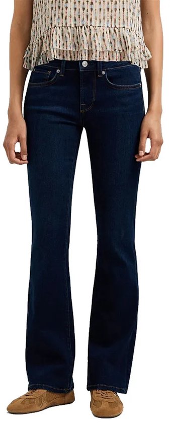Voorkant van donkerblauwe bootcut jeans met lage taille op model met beige suède sneakers.