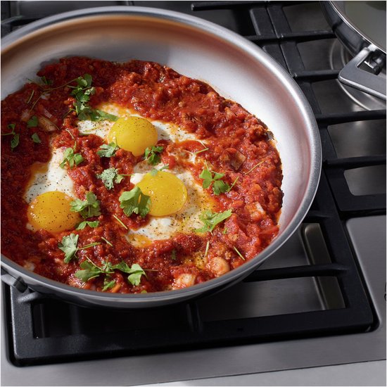 Roestvrijstalen koekenpan met shakshuka en koriander, op een gasfornuis.