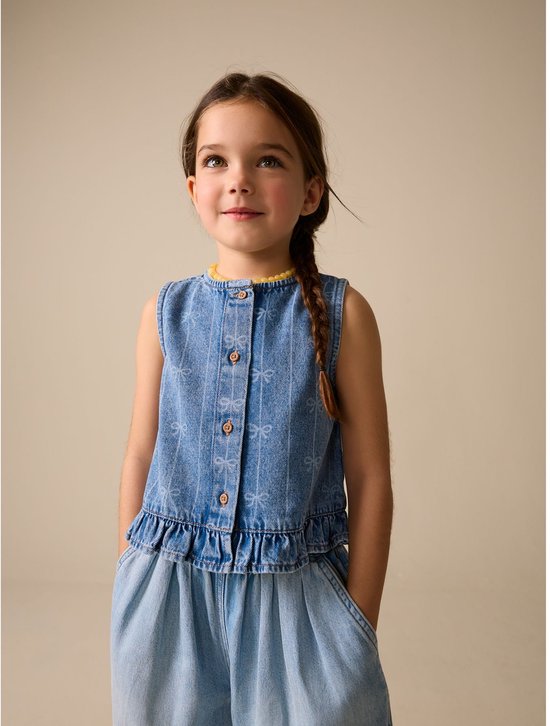 Meisje met gebloemde vlecht, draagt een mouwloos denim gilet met strikprint en wijde spijkerbroek.