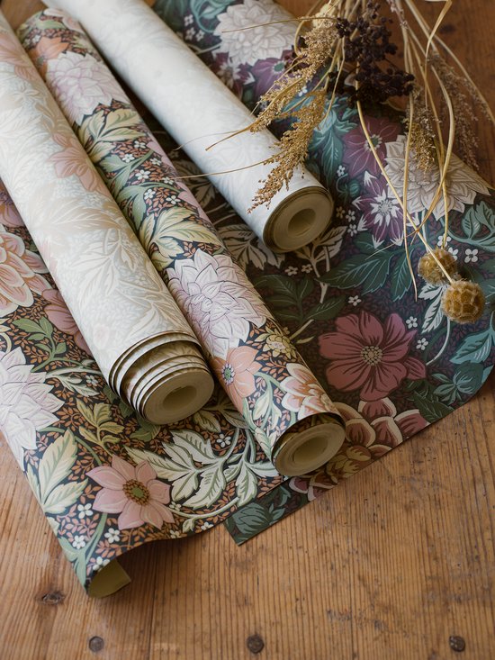 Drie rollen behang met bloemenpatroon in verschillende kleurstellingen: groen/roze, beige/roze en paars/groen.