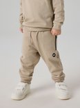Jongen in beige joggingbroek met ritszak en logoprint, en bijpassende sweater.