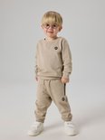 Jongen in beige joggingbroek en sweater, met bril en witte schoenen.