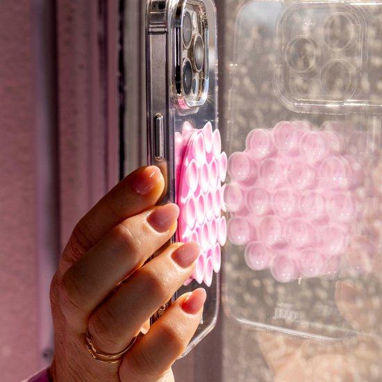 Roze telefoonsticker met zuignapjes, bevestigd aan een clear telefoonhoesje dat door een hand wordt vastgehouden.