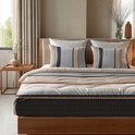 Bed opgemaakt met dekbed en kussens, met horizontale strepen in beige, bruin, grijs en wit, en een ruitpatroon.