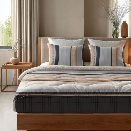 Bed opgemaakt met dekbed en kussens, met horizontale strepen in beige, bruin, grijs en wit, en een ruitpatroon.