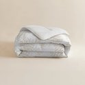 Een gevouwen wit dekbed met beige bladmotieven, op een lichte achtergrond.