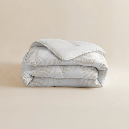 Een gevouwen wit dekbed met beige bladmotieven, op een lichte achtergrond.
