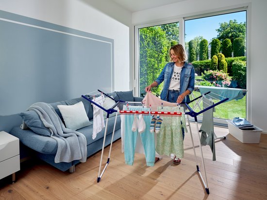 Een vrouw plaatst kleding op een wit droogrek met blauwe accenten.
