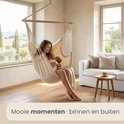 Vrouw met baby in een crèmekleurige hangstoel in een woonkamer.