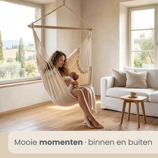 Vrouw met baby in een crèmekleurige hangstoel in een woonkamer.