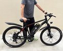 Man in grijs T-shirt staat naast een zwarte elektrische mountainbike met rode accenten.