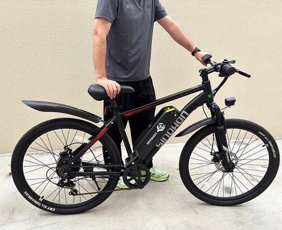 Man in grijs T-shirt staat naast een zwarte elektrische mountainbike met rode accenten.
