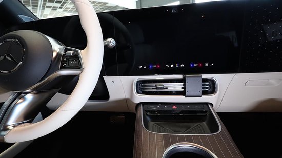 Interieur van een auto met een wit stuur, een groot zwart scherm met pictogrammen, en een zilveren ventilatierooster.